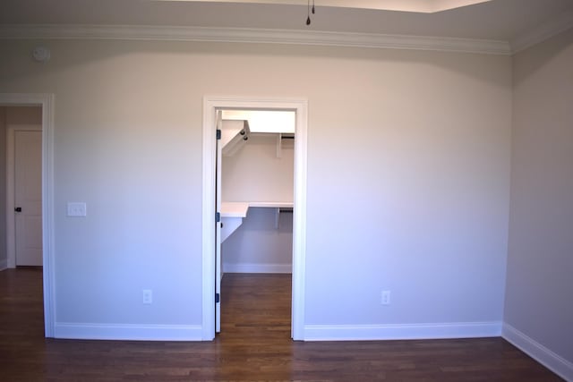 unfurnished bedroom with a walk in closet, ornamental molding, dark wood-style floors, and baseboards