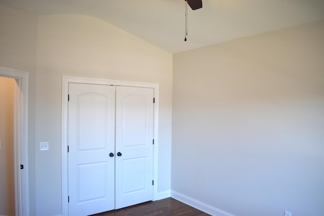 unfurnished bedroom with a closet, dark wood-type flooring, a ceiling fan, vaulted ceiling, and baseboards