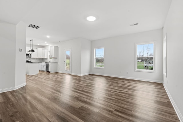 unfurnished living room featuring dark wood-style floors, visible vents, and a healthy amount of sunlight