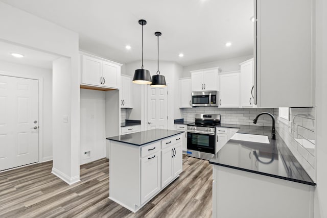 kitchen with a sink, white cabinetry, appliances with stainless steel finishes, light wood-type flooring, and dark countertops