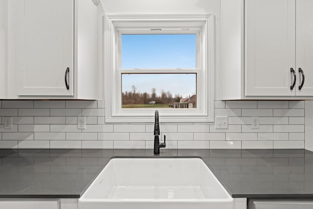 kitchen featuring decorative backsplash, dark countertops, a sink, and white cabinets