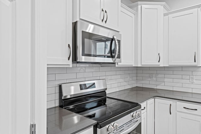 kitchen featuring stainless steel appliances, dark countertops, backsplash, and white cabinets