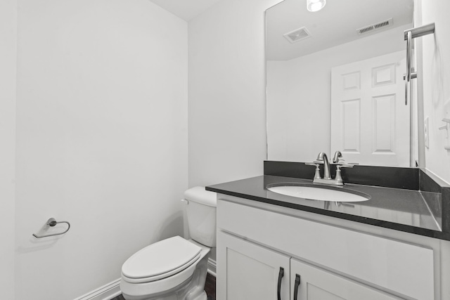 half bath featuring toilet, vanity, visible vents, and baseboards