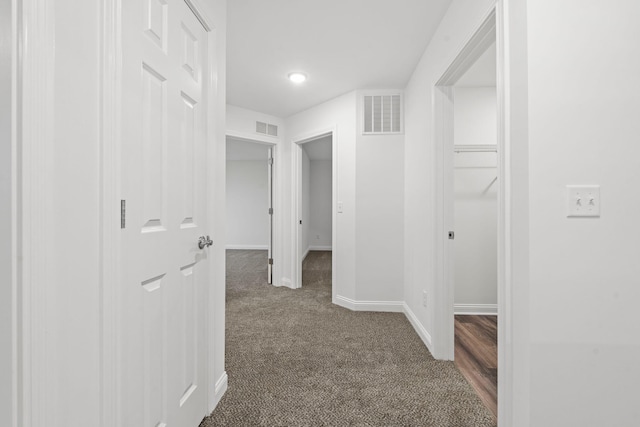 corridor with dark colored carpet, visible vents, and baseboards