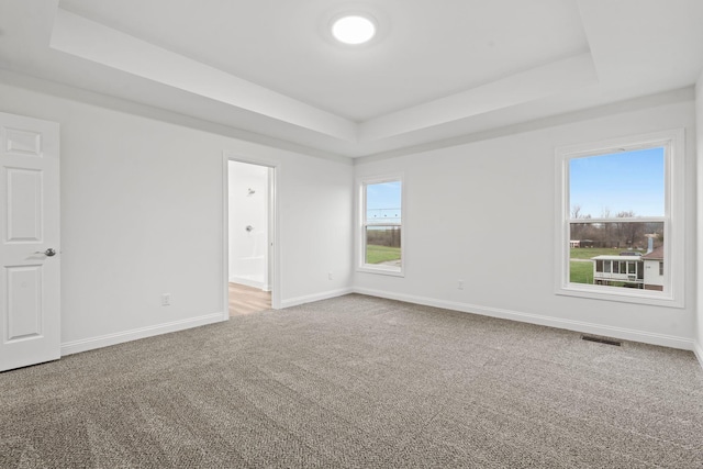 carpeted empty room featuring a raised ceiling, visible vents, and baseboards