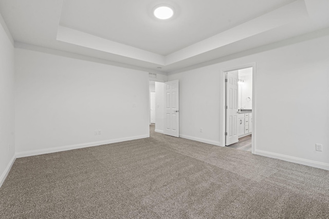 unfurnished bedroom featuring carpet floors, a tray ceiling, connected bathroom, and baseboards