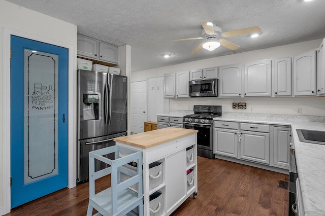 kitchen featuring ceiling fan, dark hardwood / wood-style flooring, a textured ceiling, gray cabinets, and appliances with stainless steel finishes