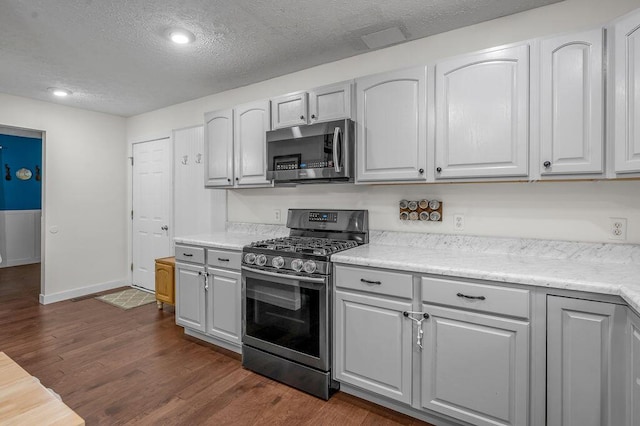 kitchen with appliances with stainless steel finishes, a textured ceiling, dark wood-type flooring, and gray cabinetry