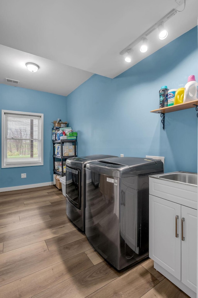 laundry room featuring separate washer and dryer, sink, rail lighting, and light hardwood / wood-style floors