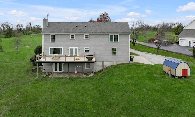 rear view of property featuring a storage unit, a yard, a wooden deck, and french doors