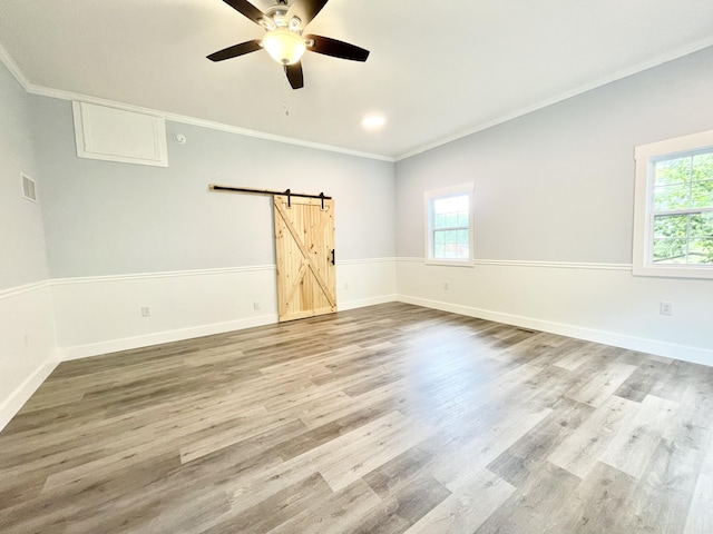 empty room with hardwood / wood-style floors, a barn door, ceiling fan, and crown molding