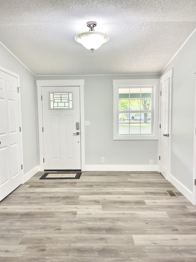 foyer with light hardwood / wood-style flooring, a textured ceiling, and ornamental molding