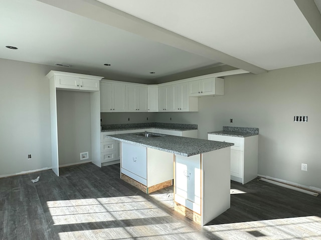 kitchen with a kitchen island, dark hardwood / wood-style flooring, stovetop, dark stone counters, and white cabinets