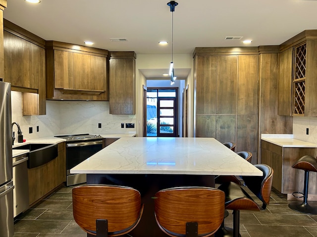 kitchen with appliances with stainless steel finishes, backsplash, light stone counters, decorative light fixtures, and a center island