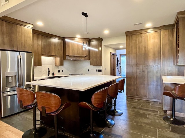 kitchen featuring hanging light fixtures, tasteful backsplash, a kitchen breakfast bar, stainless steel fridge with ice dispenser, and a kitchen island