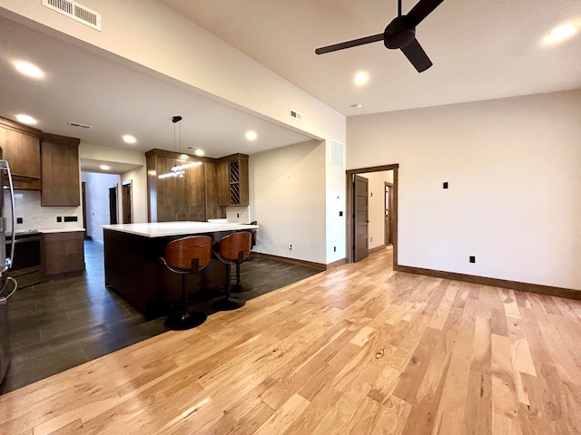 kitchen with tasteful backsplash, a breakfast bar, ceiling fan, pendant lighting, and hardwood / wood-style flooring