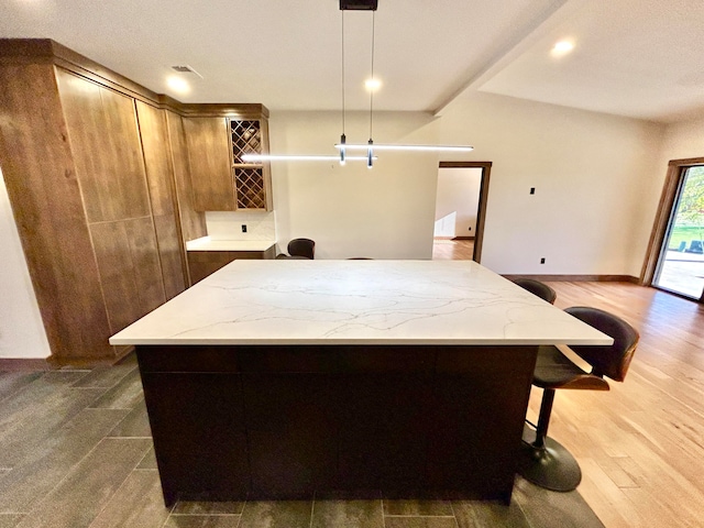 kitchen with decorative light fixtures, dark wood-type flooring, light stone countertops, and a kitchen island