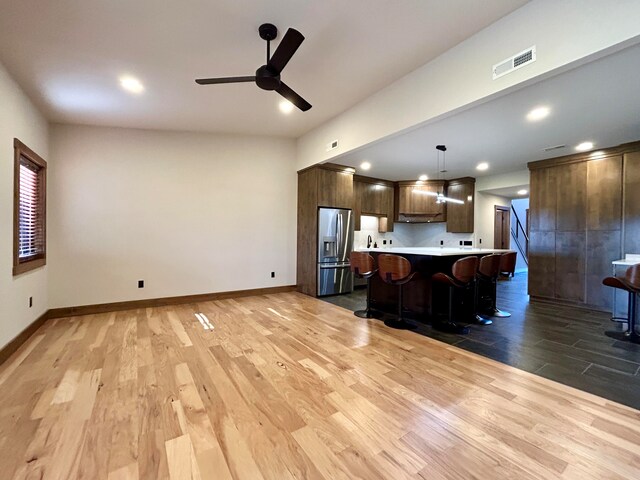 kitchen featuring hanging light fixtures, stainless steel refrigerator with ice dispenser, a kitchen island, light hardwood / wood-style floors, and a kitchen bar