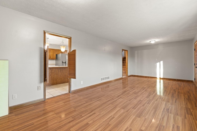 spare room with a textured ceiling and light hardwood / wood-style flooring