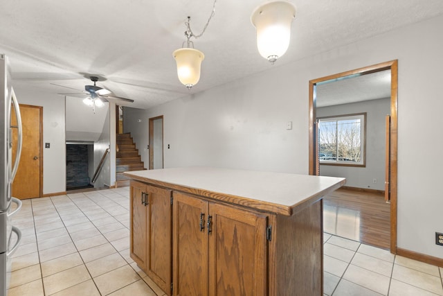 kitchen featuring decorative light fixtures, a center island, a textured ceiling, light tile patterned floors, and stainless steel refrigerator