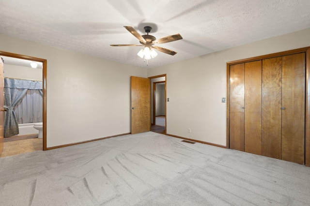 unfurnished bedroom with a closet, ensuite bathroom, light carpet, and a textured ceiling