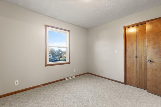 unfurnished bedroom featuring a closet, light carpet, and a textured ceiling