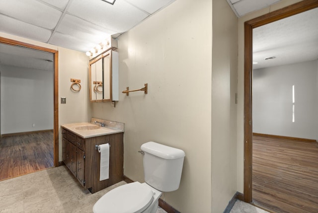 bathroom featuring a drop ceiling, vanity, wood-type flooring, and toilet