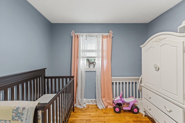 bedroom with light wood-type flooring and a nursery area