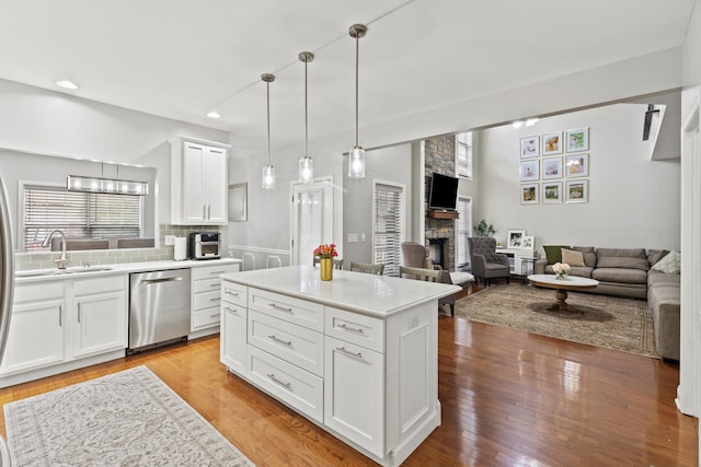 kitchen featuring white cabinetry, dishwasher, a center island, a stone fireplace, and light hardwood / wood-style floors