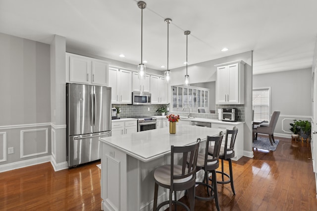 kitchen with a kitchen bar, appliances with stainless steel finishes, dark hardwood / wood-style flooring, pendant lighting, and a kitchen island