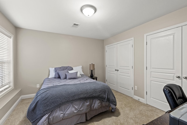 bedroom featuring light colored carpet and multiple closets