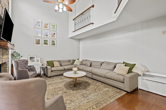 living room with dark hardwood / wood-style floors, ceiling fan, a fireplace, and a high ceiling