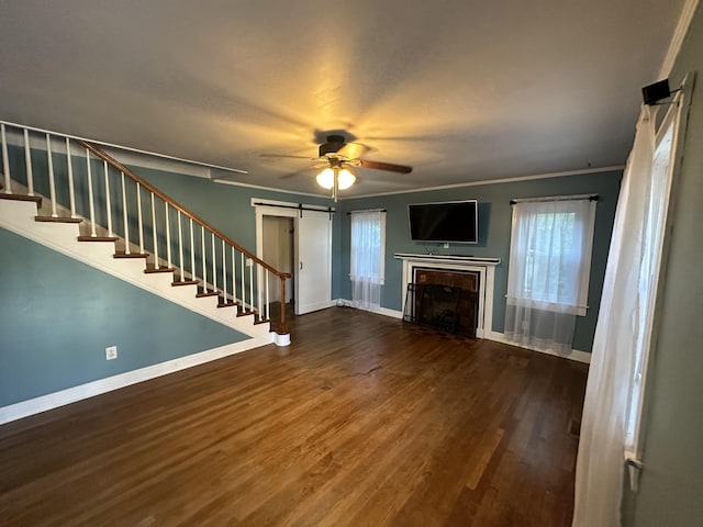 unfurnished living room featuring a barn door, ceiling fan, dark hardwood / wood-style flooring, and ornamental molding