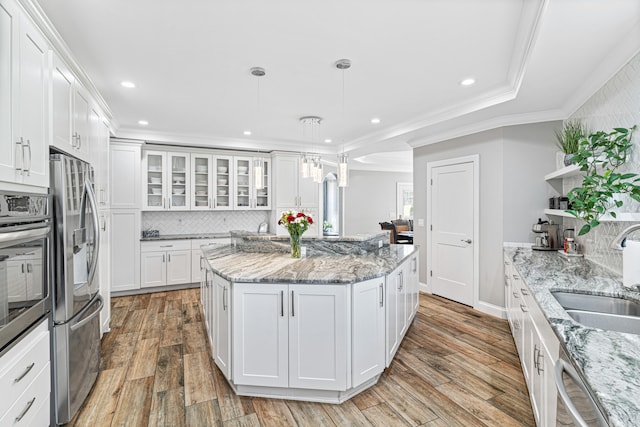 kitchen with light stone counters, sink, wood-type flooring, decorative light fixtures, and white cabinetry