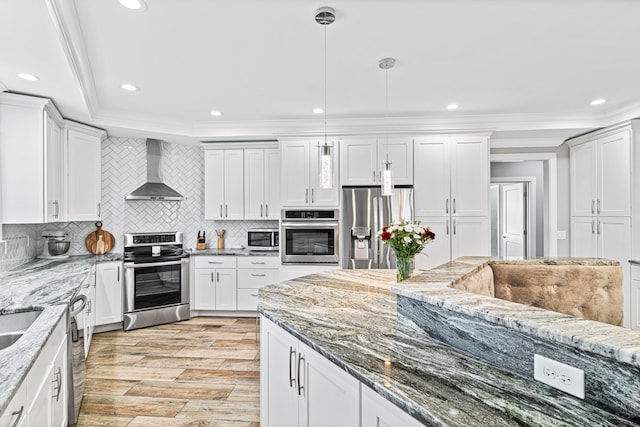 kitchen featuring wall chimney range hood, hanging light fixtures, light stone countertops, appliances with stainless steel finishes, and white cabinetry