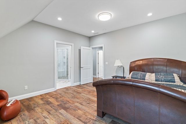 bedroom featuring hardwood / wood-style flooring, ensuite bathroom, and lofted ceiling