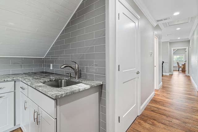 kitchen featuring white cabinets, sink, vaulted ceiling, light stone countertops, and light wood-type flooring