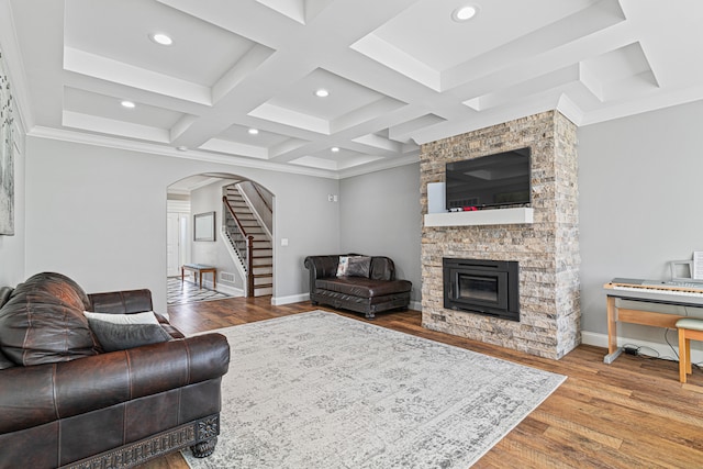 living room with ornamental molding, coffered ceiling, beamed ceiling, light hardwood / wood-style floors, and a stone fireplace