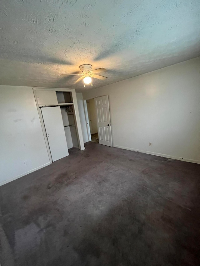 unfurnished bedroom featuring ceiling fan, dark carpet, and a textured ceiling