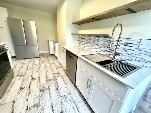 kitchen with light stone counters, backsplash, appliances with stainless steel finishes, white cabinets, and light wood-type flooring