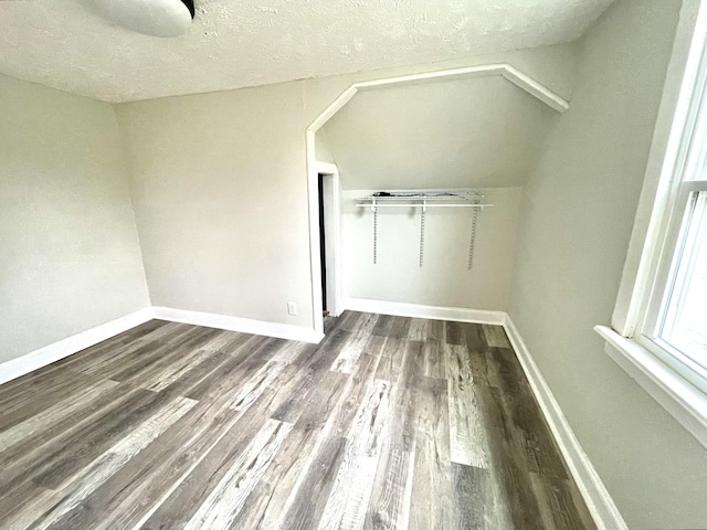 unfurnished bedroom featuring a textured ceiling, dark hardwood / wood-style flooring, and lofted ceiling