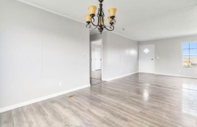 spare room featuring hardwood / wood-style flooring, crown molding, and a notable chandelier