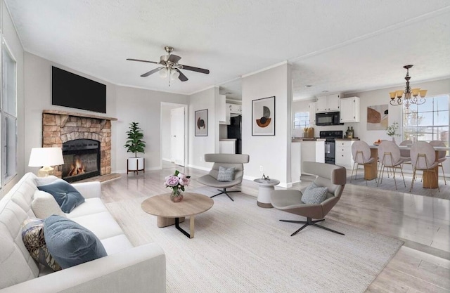 living room with a stone fireplace, crown molding, ceiling fan with notable chandelier, and light wood-type flooring