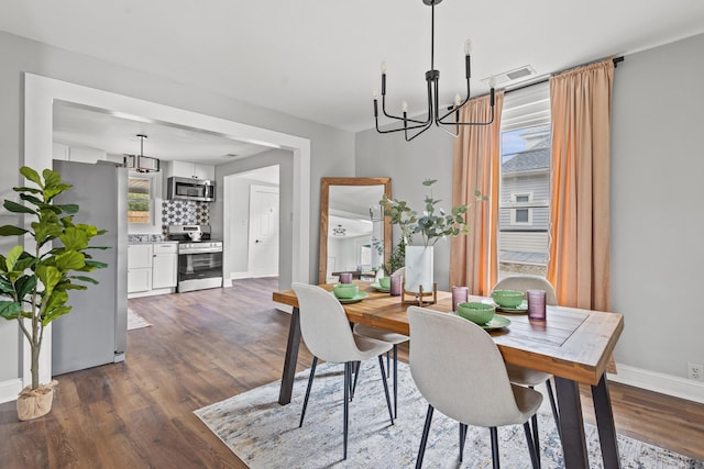 dining room featuring dark wood-type flooring, a healthy amount of sunlight, and a notable chandelier