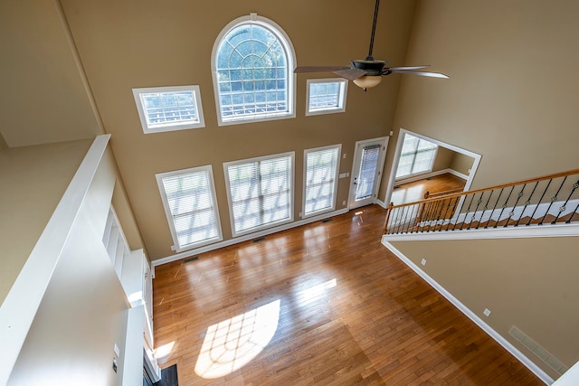 unfurnished living room featuring ceiling fan, a high ceiling, and hardwood / wood-style flooring