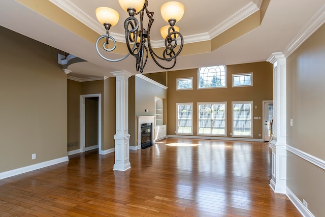 unfurnished living room with ornate columns, hardwood / wood-style floors, a chandelier, and ornamental molding