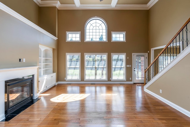 unfurnished living room featuring light hardwood / wood-style floors, built in features, and crown molding