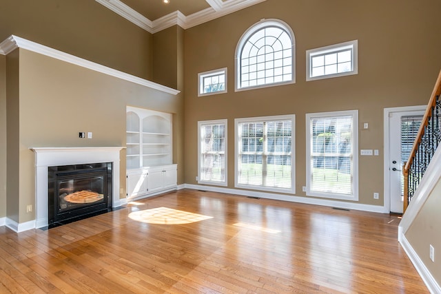 unfurnished living room featuring crown molding, light hardwood / wood-style flooring, a towering ceiling, and built in features