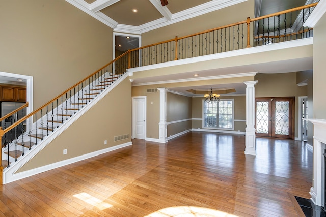 unfurnished living room with a notable chandelier, wood-type flooring, a towering ceiling, and crown molding