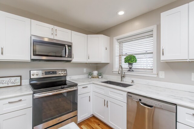 kitchen featuring white cabinetry, stainless steel dishwasher, light stone counters, and sink